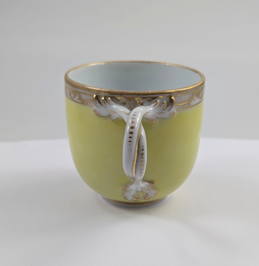 An antique nineteenth-century Meissen porcelain demitasse cup and saucer in yellow featuring hand-painted pastoral scenes set within intricate gilded cartouches. View VI