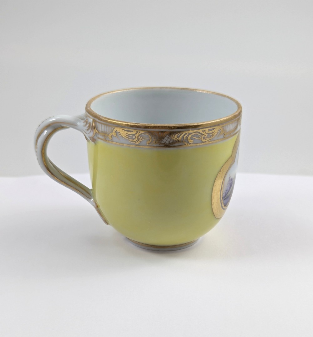 An antique nineteenth-century Meissen porcelain demitasse cup and saucer in yellow featuring hand-painted pastoral scenes set within intricate gilded cartouches. View VII