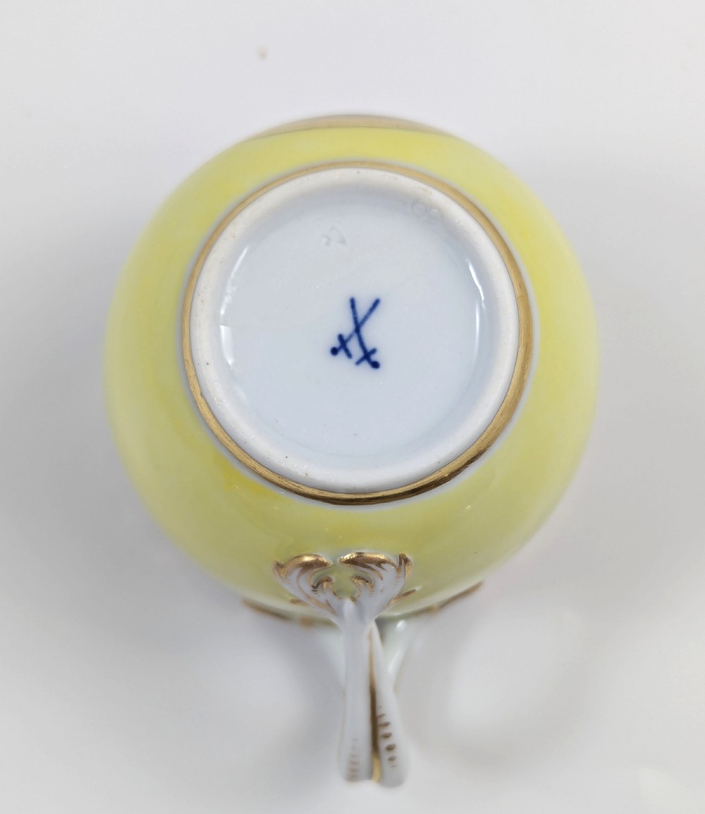 An antique nineteenth-century Meissen porcelain demitasse cup and saucer in yellow featuring hand-painted pastoral scenes set within intricate gilded cartouches. View X