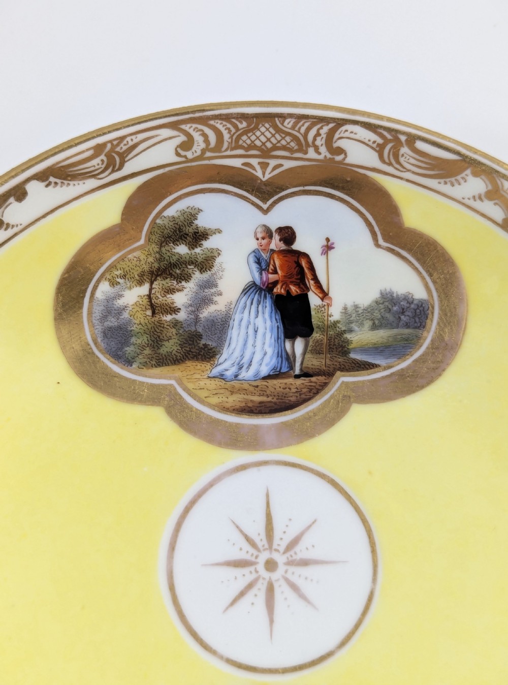 An antique nineteenth-century Meissen porcelain demitasse cup and saucer in yellow featuring hand-painted pastoral scenes set within intricate gilded cartouches. View XIV