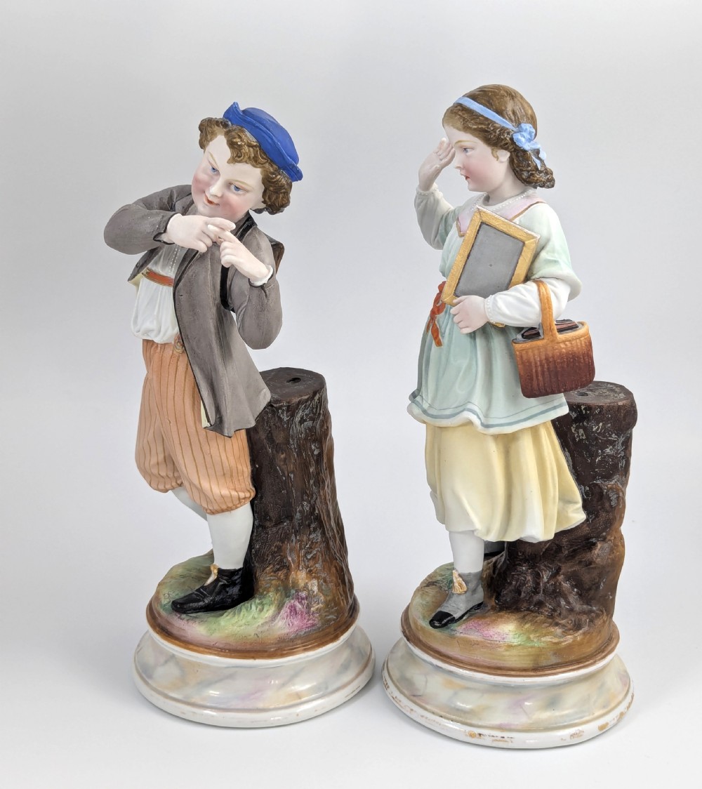A pair of 19th-century French bisque porcelain figurines depicting a schoolboy and girl in traditional attire on round bases. View II