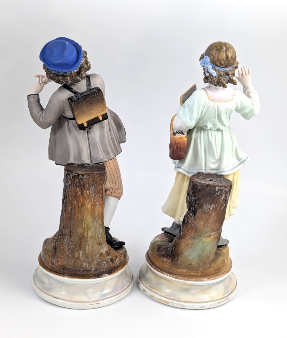 A pair of 19th-century French bisque porcelain figurines depicting a schoolboy and girl in traditional attire on round bases. View III