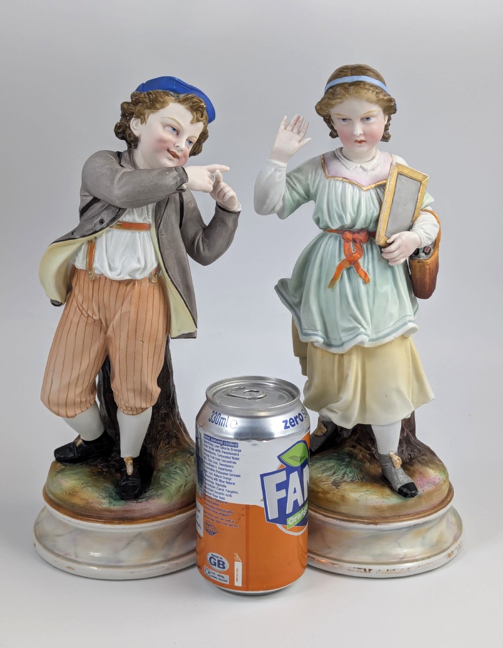 A pair of 19th-century French bisque porcelain figurines depicting a schoolboy and girl in traditional attire on round bases. View VIII