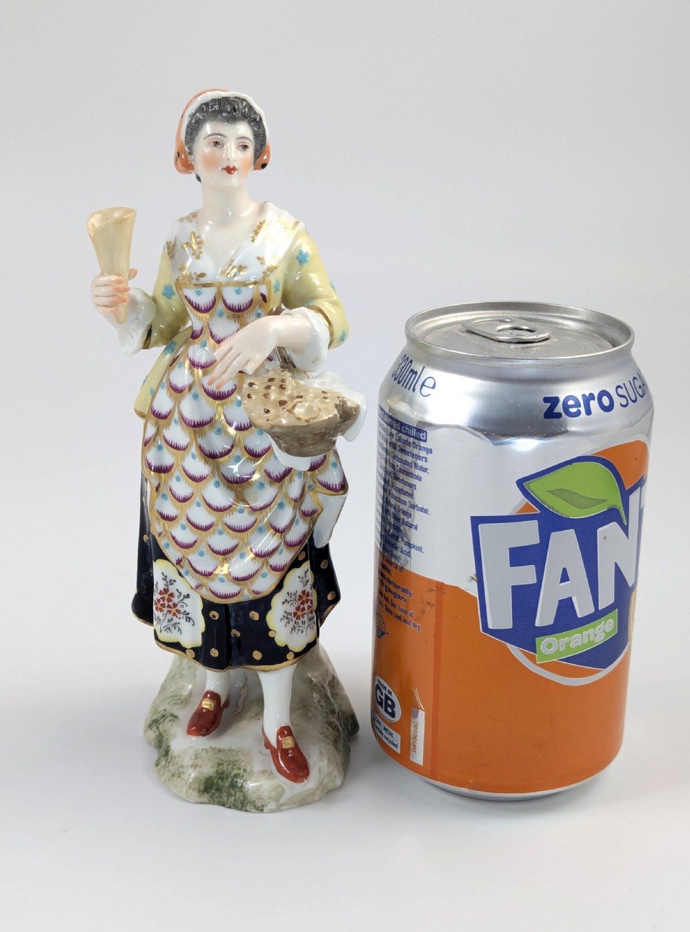 A nineteenth-century Samson of Paris porcelain figurine depicting a female street seller in decorated attire holding a basket and a cone. View IX