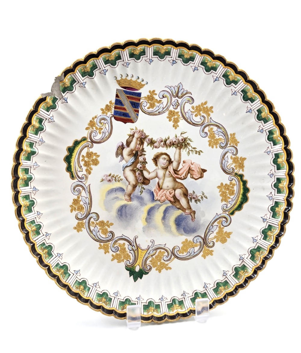 A pair of 18th-century French tin-glazed earthenware display plates with hand-painted putti motifs, armorial shields, and green scalloped borders. View II
