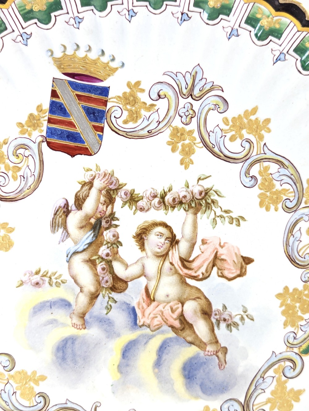 A pair of 18th-century French tin-glazed earthenware display plates with hand-painted putti motifs, armorial shields, and green scalloped borders. View IV
