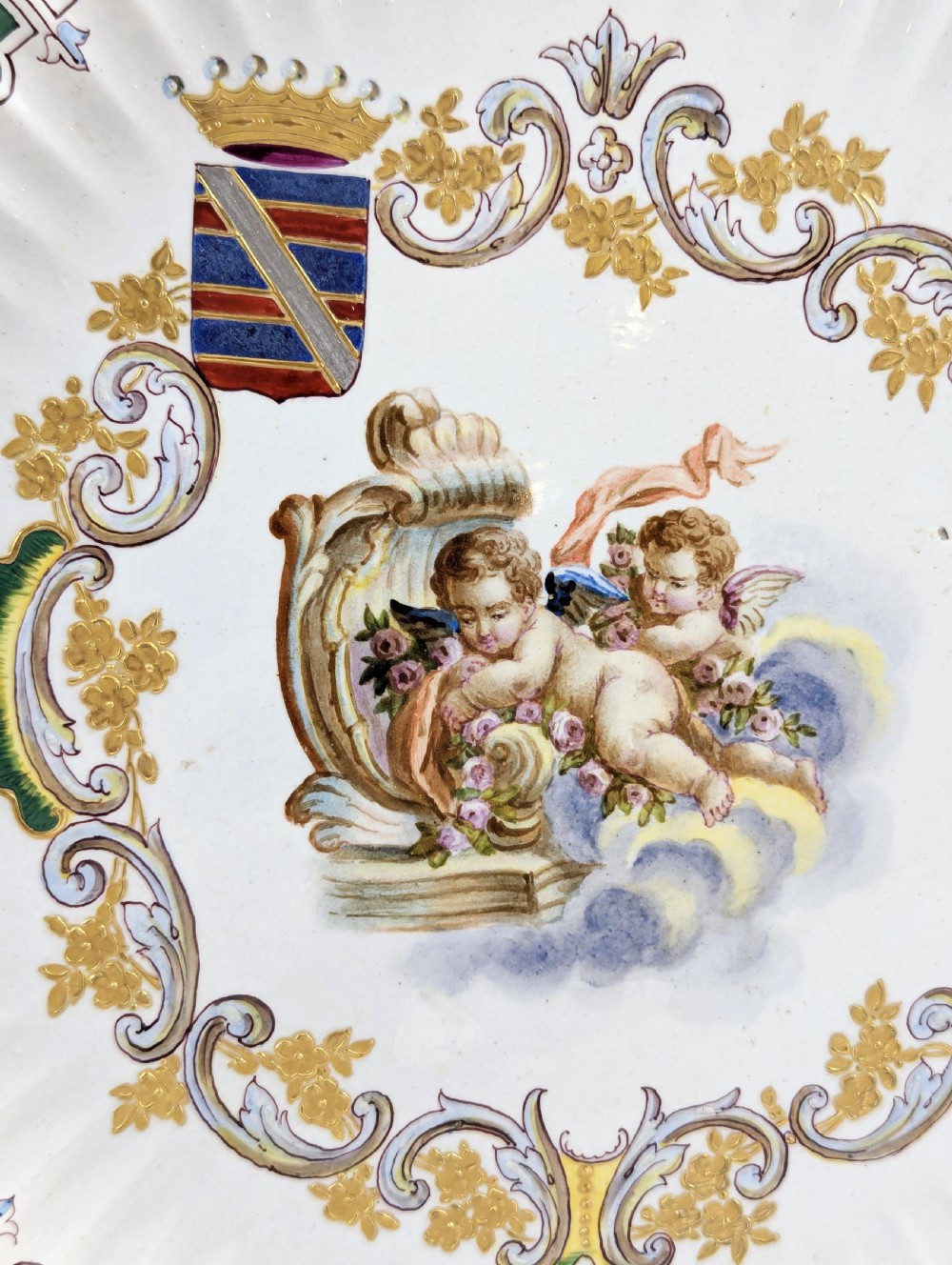 A pair of 18th-century French tin-glazed earthenware display plates with hand-painted putti motifs, armorial shields, and green scalloped borders. View VII