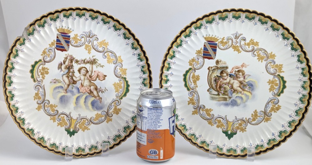 A pair of 18th-century French tin-glazed earthenware display plates with hand-painted putti motifs, armorial shields, and green scalloped borders. View IX
