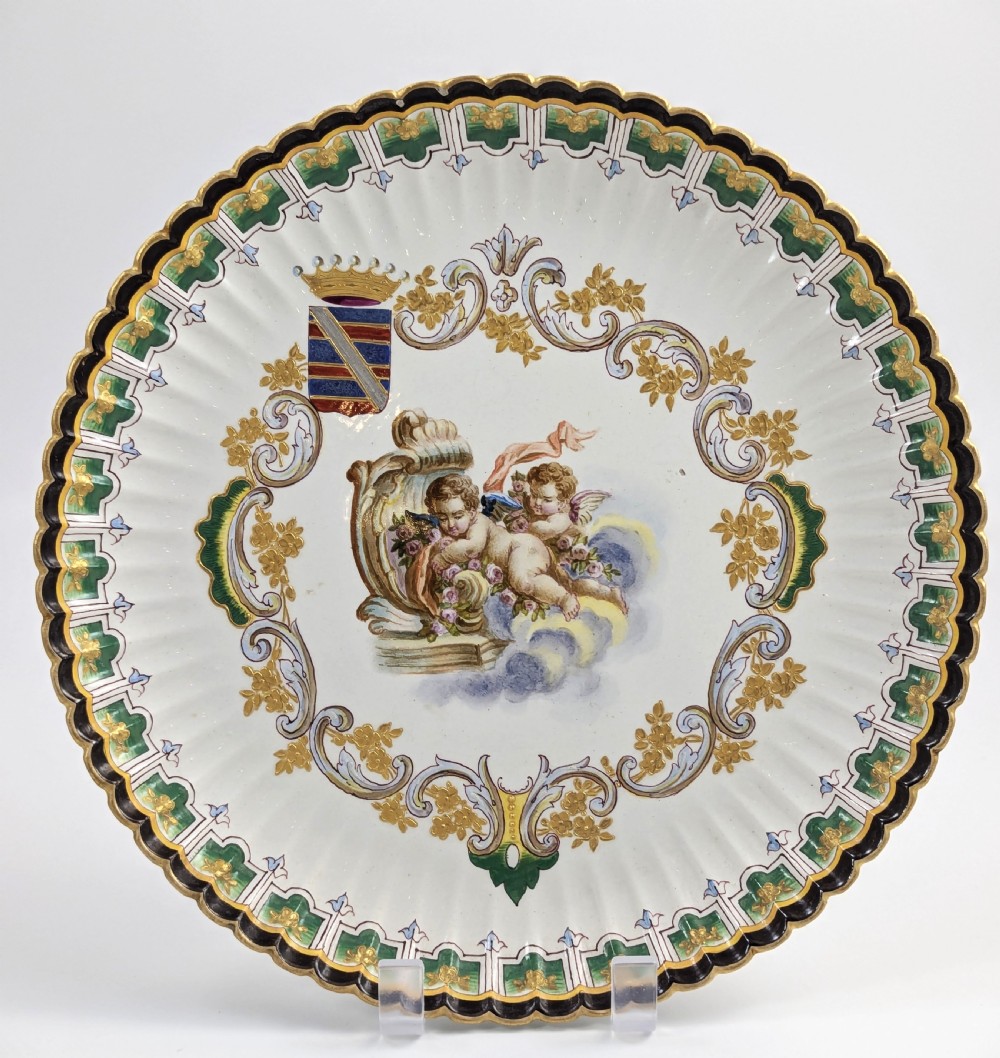 A pair of 18th-century French tin-glazed earthenware display plates with hand-painted putti motifs, armorial shields, and green scalloped borders. View XI