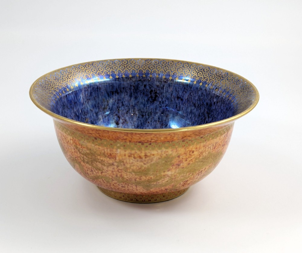 A circular ceramic bowl displaying a mottled orange and gold exterior with a deep speckled blue interior bordered by detailed gilt geometric patterns.