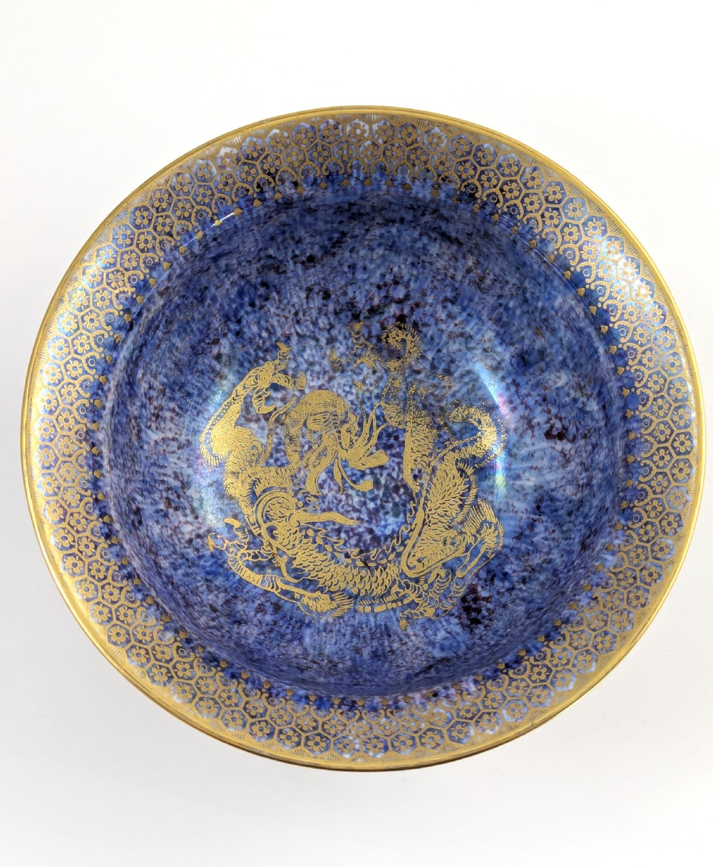 A circular ceramic bowl displaying a mottled orange and gold exterior with a deep speckled blue interior bordered by detailed gilt geometric patterns. View V