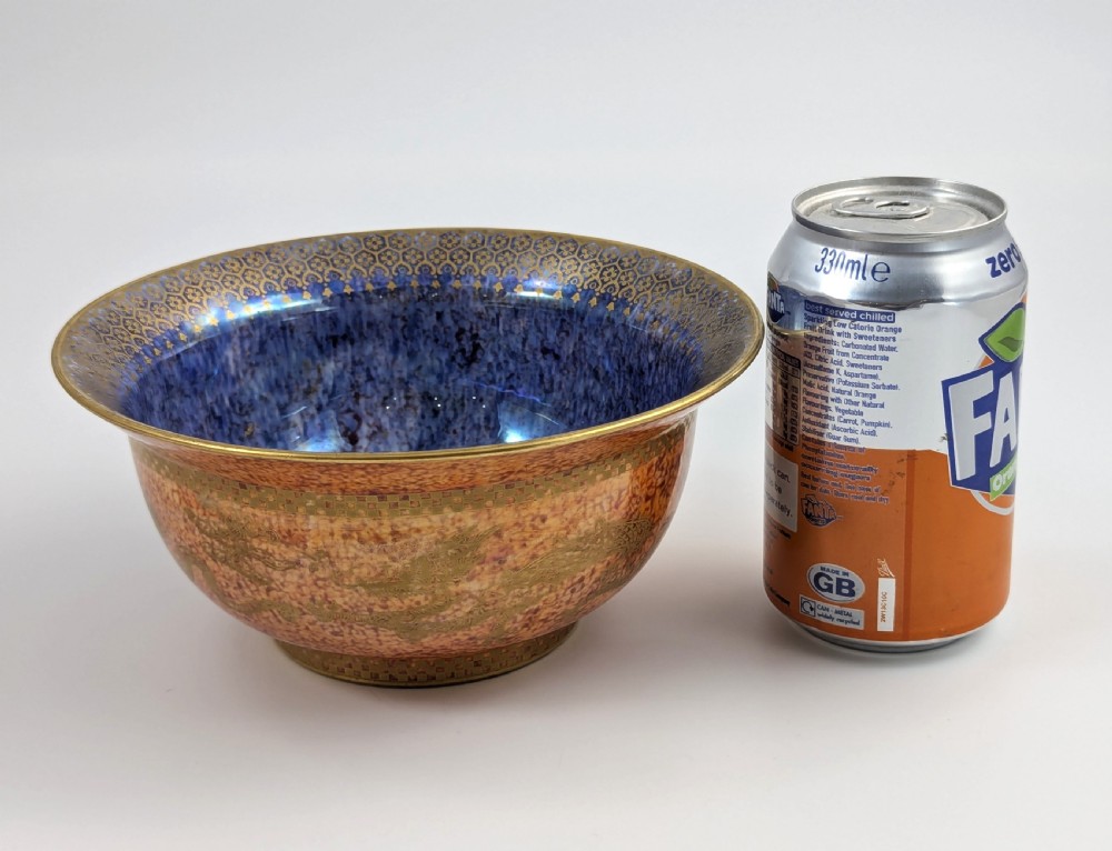 A circular ceramic bowl displaying a mottled orange and gold exterior with a deep speckled blue interior bordered by detailed gilt geometric patterns. View X