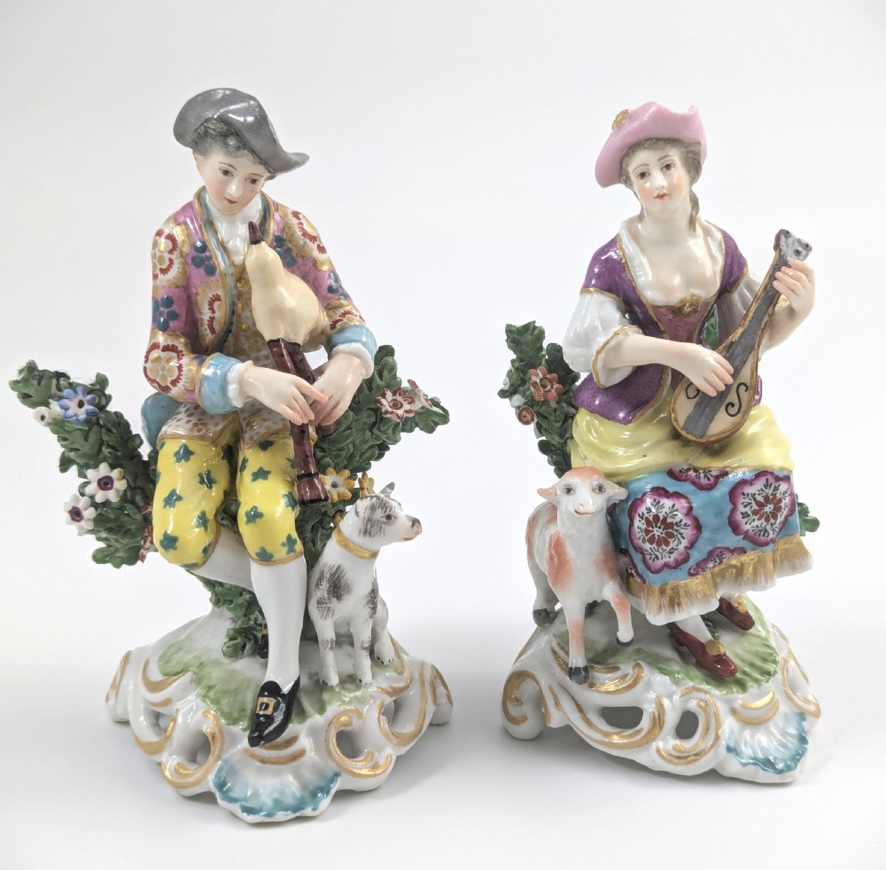 Pair of nineteenth-century Dresden porcelain figurines depicting a male bagpipe player with a dog and a female lute player with a lamb, both styled in Rococo attire on ornate bases.