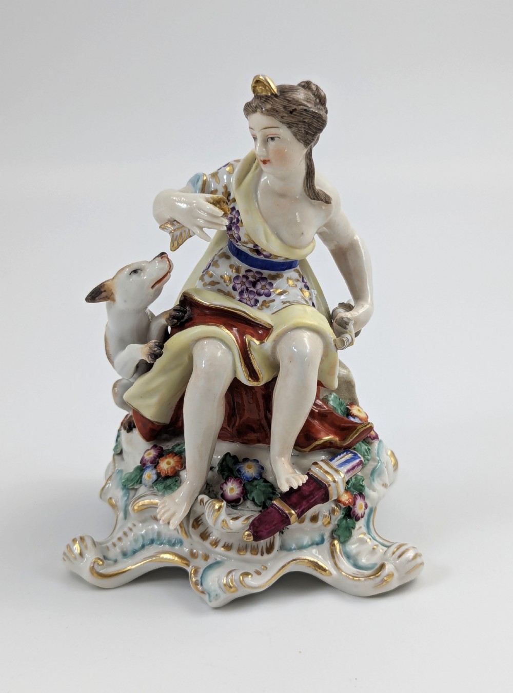 An 18th-century Chelsea soft-paste porcelain figurine depicting Diana the Huntress seated on a Rococo scroll base with a hound and quiver.