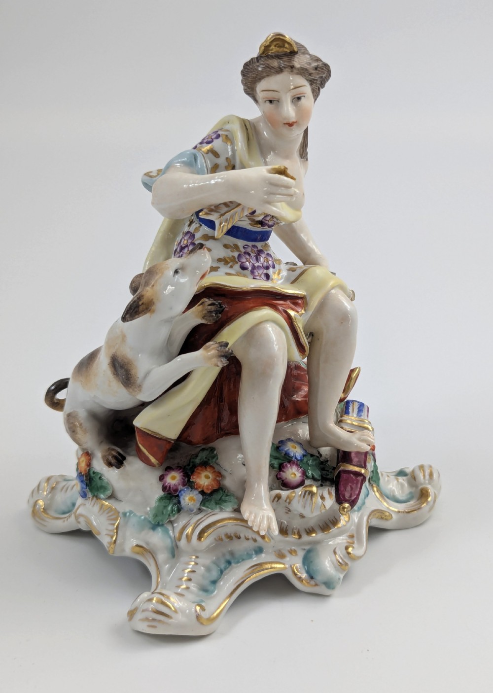An 18th-century Chelsea soft-paste porcelain figurine depicting Diana the Huntress seated on a Rococo scroll base with a hound and quiver. View II
