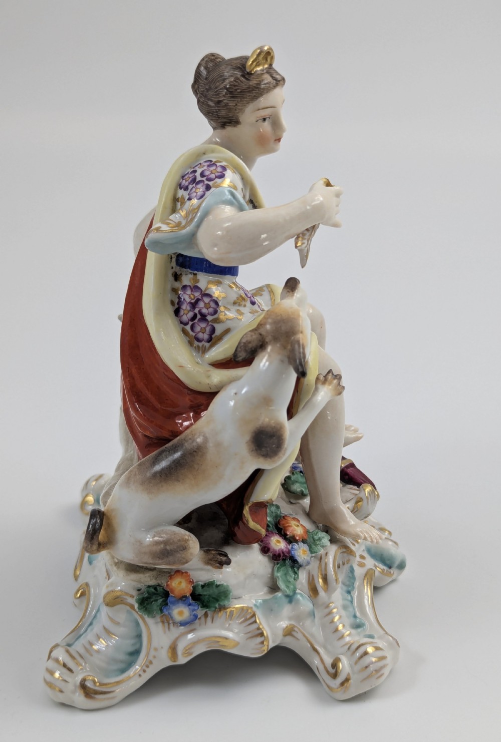 An 18th-century Chelsea soft-paste porcelain figurine depicting Diana the Huntress seated on a Rococo scroll base with a hound and quiver. View III