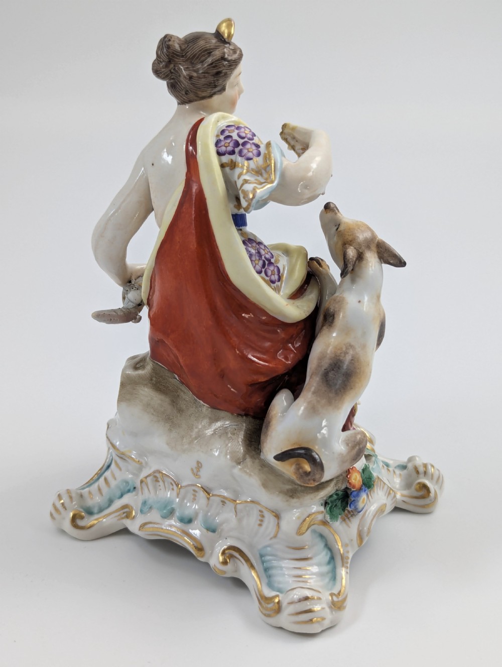 An 18th-century Chelsea soft-paste porcelain figurine depicting Diana the Huntress seated on a Rococo scroll base with a hound and quiver. View V