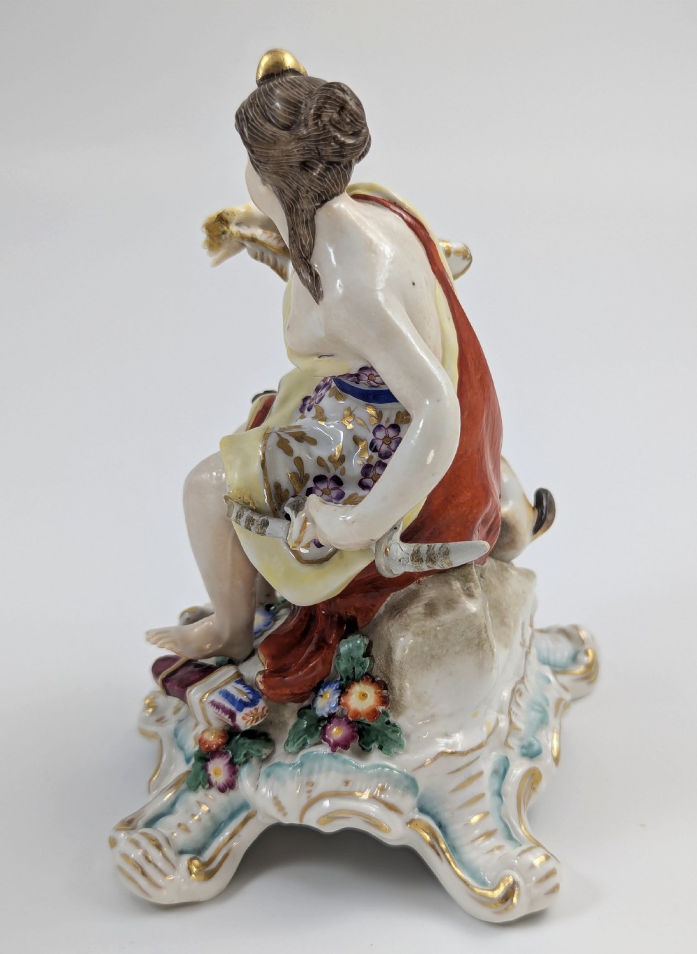 An 18th-century Chelsea soft-paste porcelain figurine depicting Diana the Huntress seated on a Rococo scroll base with a hound and quiver. View VI