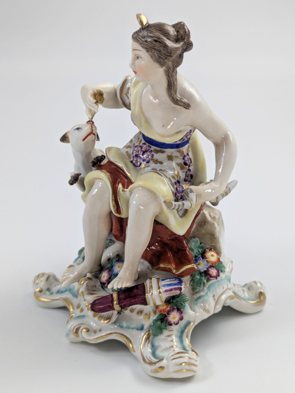 An 18th-century Chelsea soft-paste porcelain figurine depicting Diana the Huntress seated on a Rococo scroll base with a hound and quiver. View VII