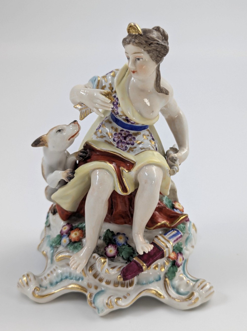 An 18th-century Chelsea soft-paste porcelain figurine depicting Diana the Huntress seated on a Rococo scroll base with a hound and quiver. View VIII