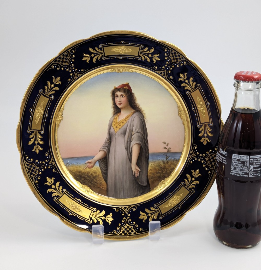 A circular porcelain cabinet plate with a central hand-painted portrait of a woman in draped attire set within a cobalt blue rim embellished with gold gilding. View VI