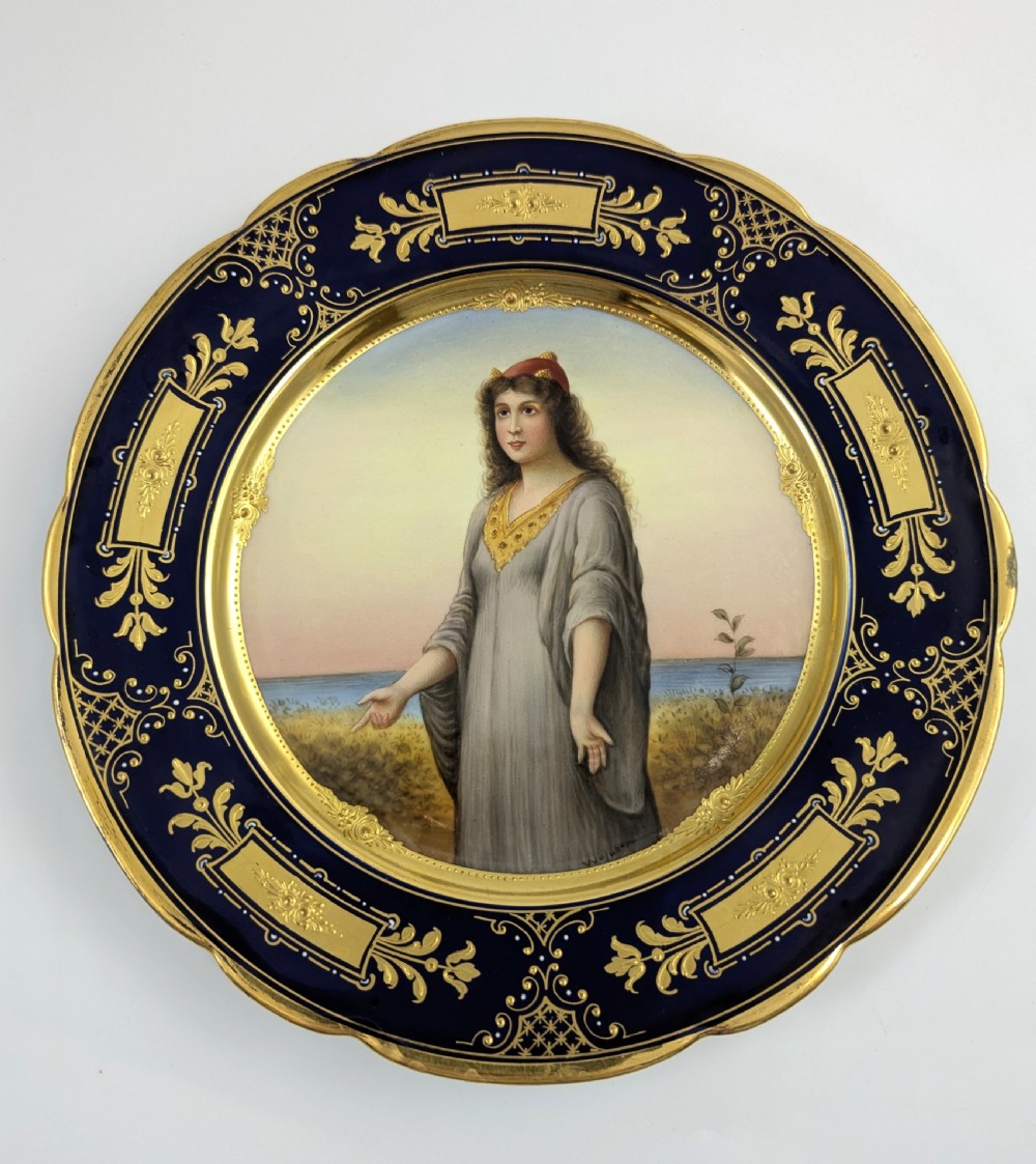 A circular porcelain cabinet plate with a central hand-painted portrait of a woman in draped attire set within a cobalt blue rim embellished with gold gilding. View VIII