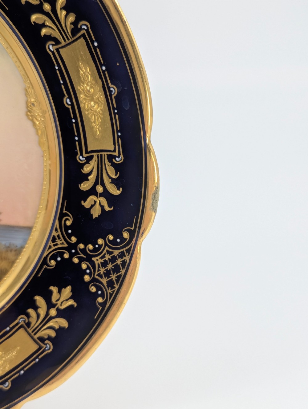A circular porcelain cabinet plate with a central hand-painted portrait of a woman in draped attire set within a cobalt blue rim embellished with gold gilding. View X