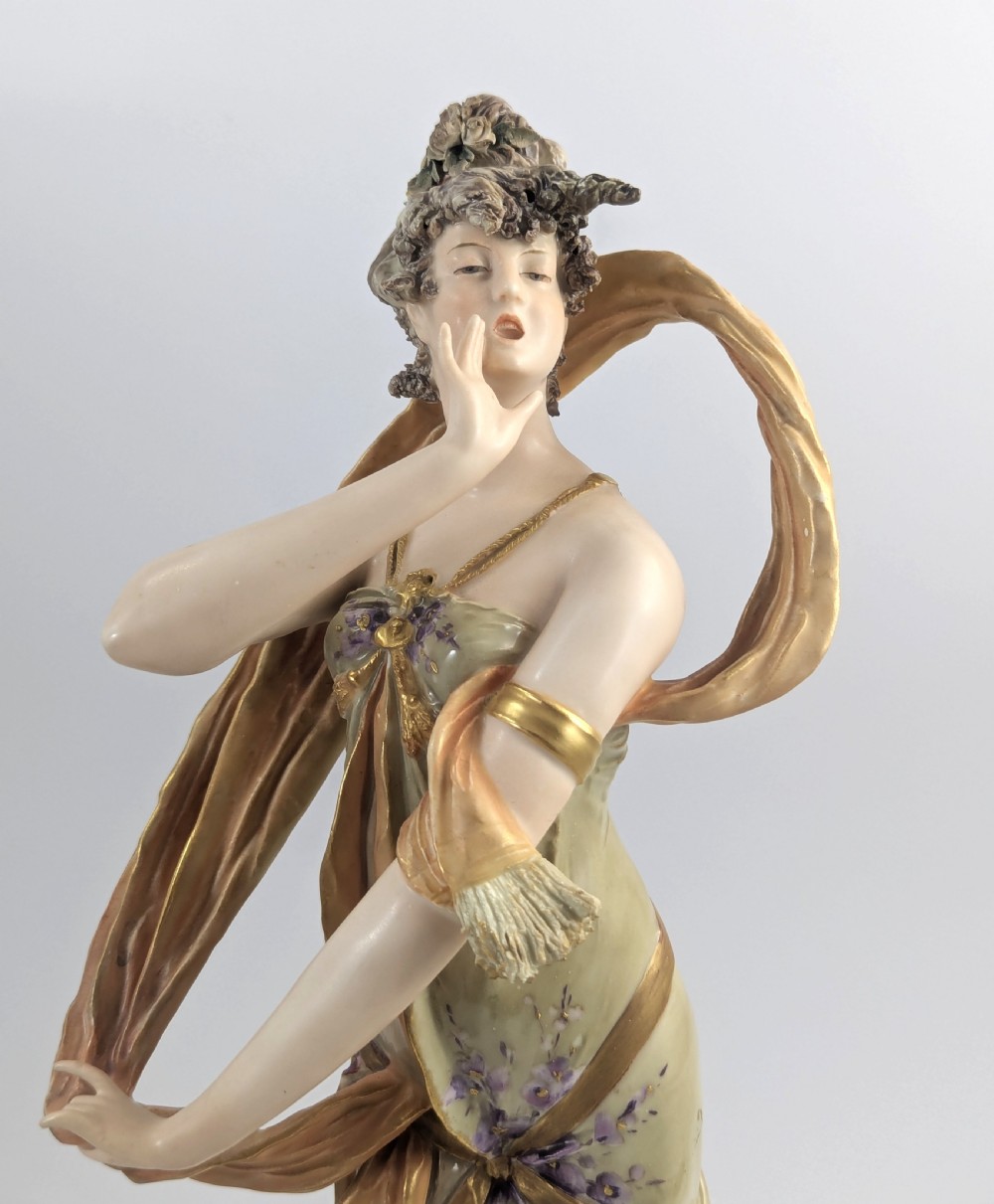 An Art Nouveau porcelain figurine depicting a standing maiden wrapped in a flowing scarf with a sage green dress on a naturalistic base. View IX