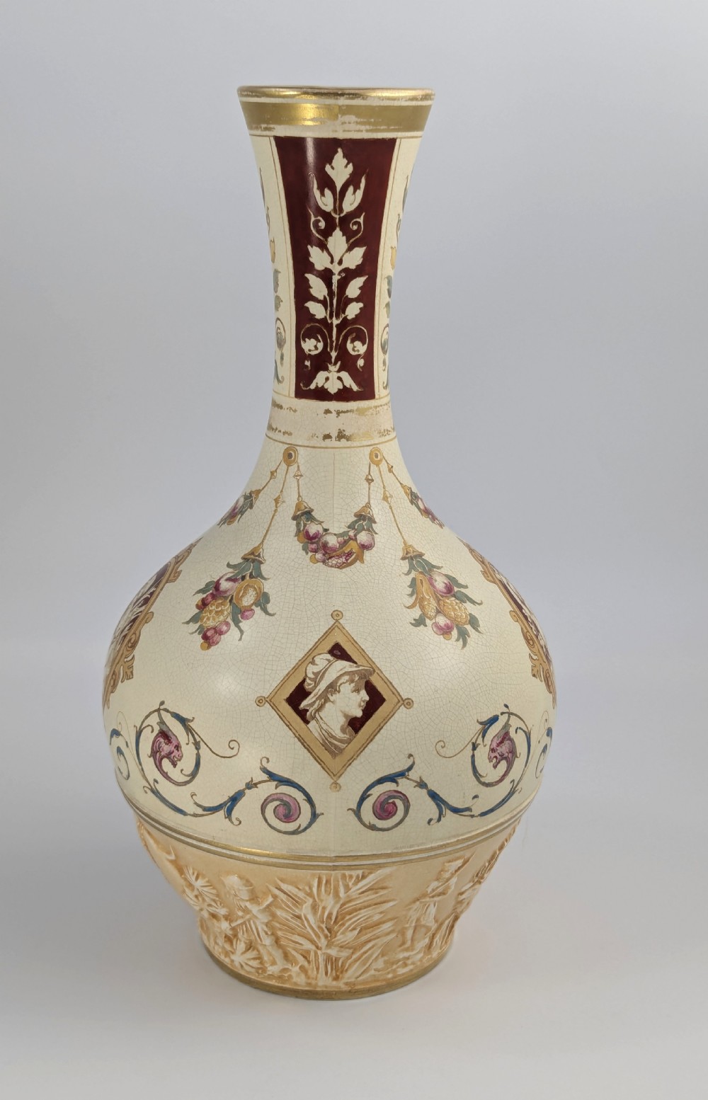 A late 19th-century Wedgwood ceramic vase featuring a slender neck, bulbous body decorated with classical cartouches and gilt details, resting on a carved relief base. View V