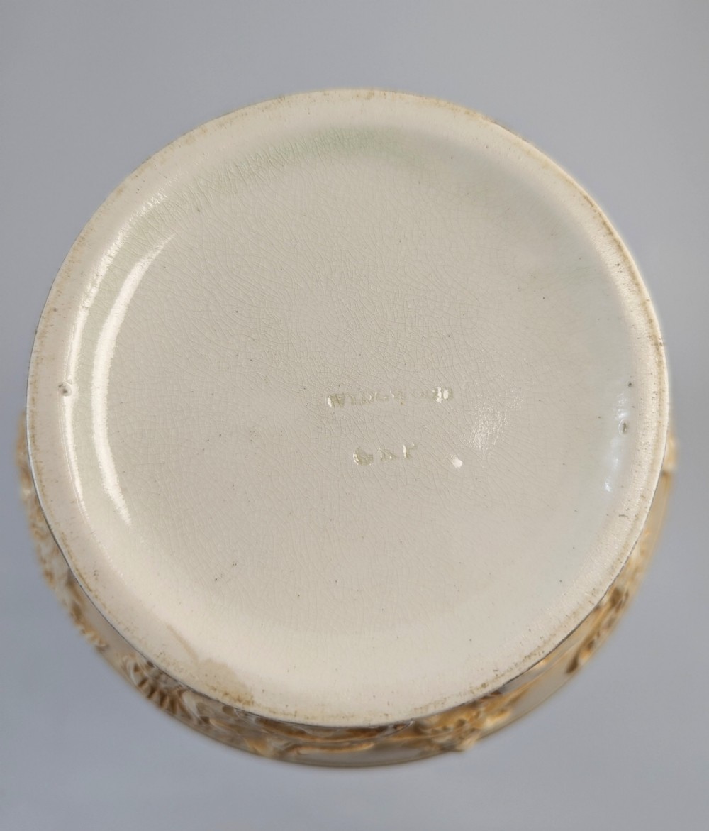 A late 19th-century Wedgwood ceramic vase featuring a slender neck, bulbous body decorated with classical cartouches and gilt details, resting on a carved relief base. View X