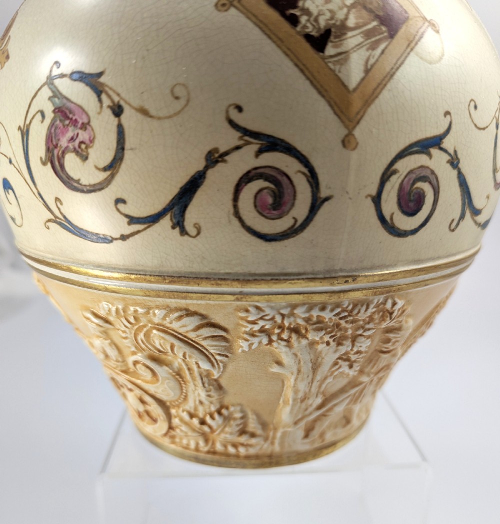 A late 19th-century Wedgwood ceramic vase featuring a slender neck, bulbous body decorated with classical cartouches and gilt details, resting on a carved relief base. View XII