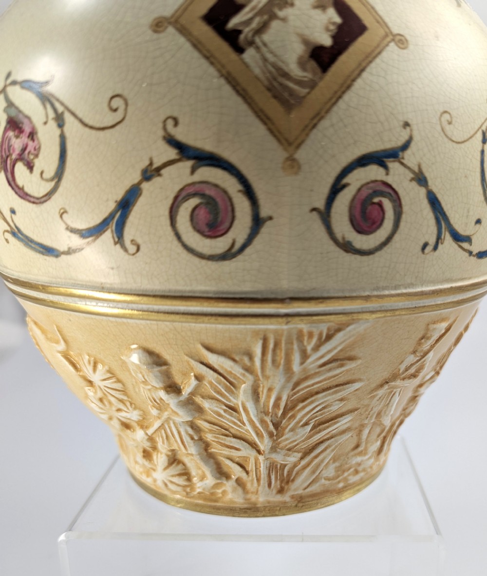 A late 19th-century Wedgwood ceramic vase featuring a slender neck, bulbous body decorated with classical cartouches and gilt details, resting on a carved relief base. View XIV