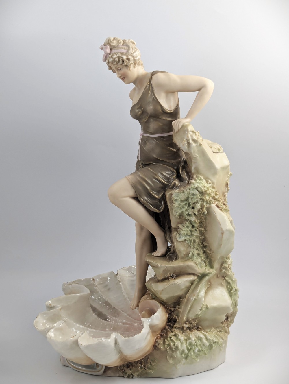 An Art Nouveau Royal Dux porcelain centrepiece depicting a draped female bather standing atop rockwork above a large shell-shaped basin. View II
