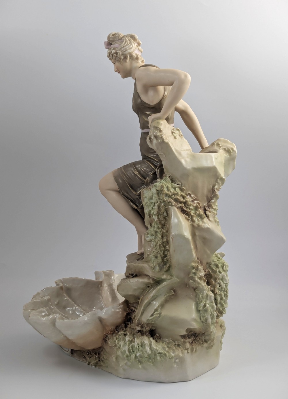 An Art Nouveau Royal Dux porcelain centrepiece depicting a draped female bather standing atop rockwork above a large shell-shaped basin. View III