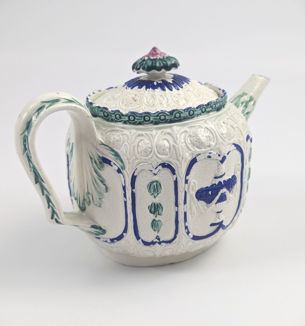 An 18th-century lead-glazed ceramic teapot featuring relief-moulded arches, blue and green painted accents, and a moulded lid with a pink flower finial. View III