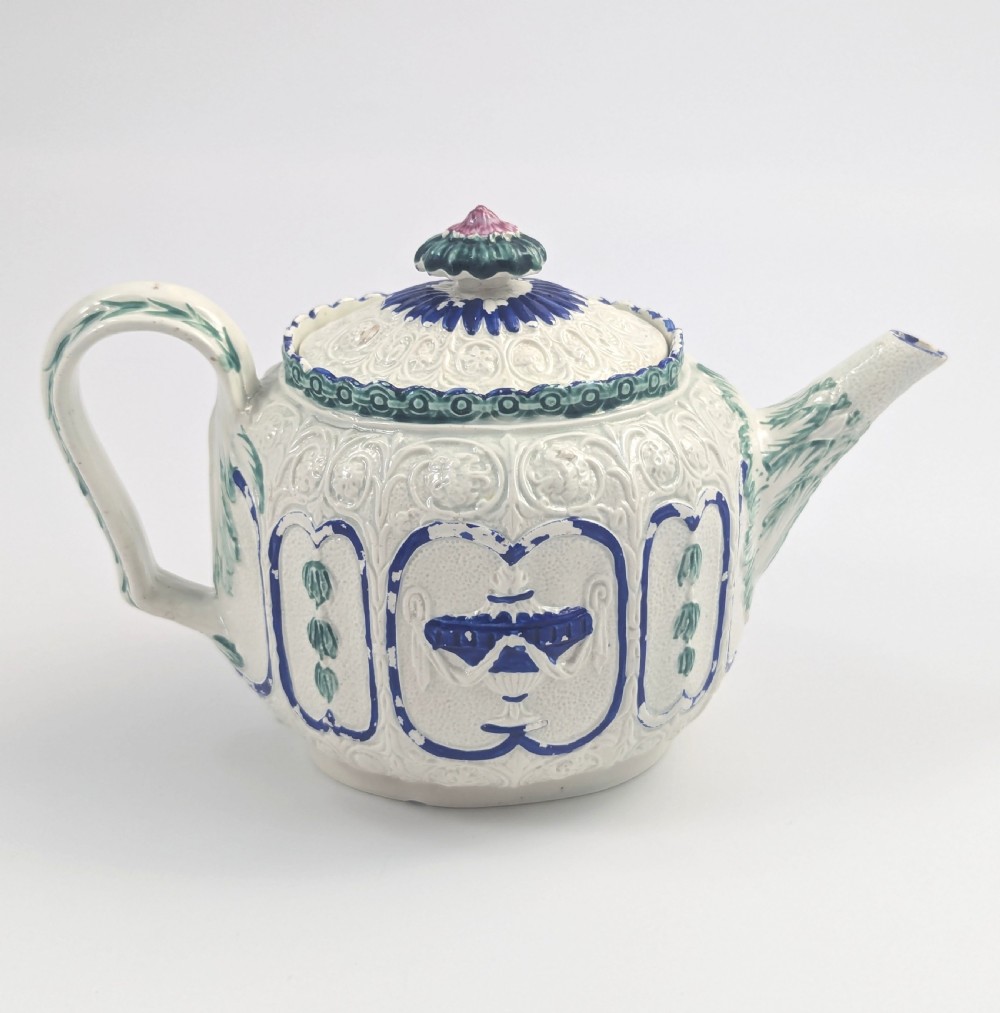 An 18th-century lead-glazed ceramic teapot featuring relief-moulded arches, blue and green painted accents, and a moulded lid with a pink flower finial. View IV