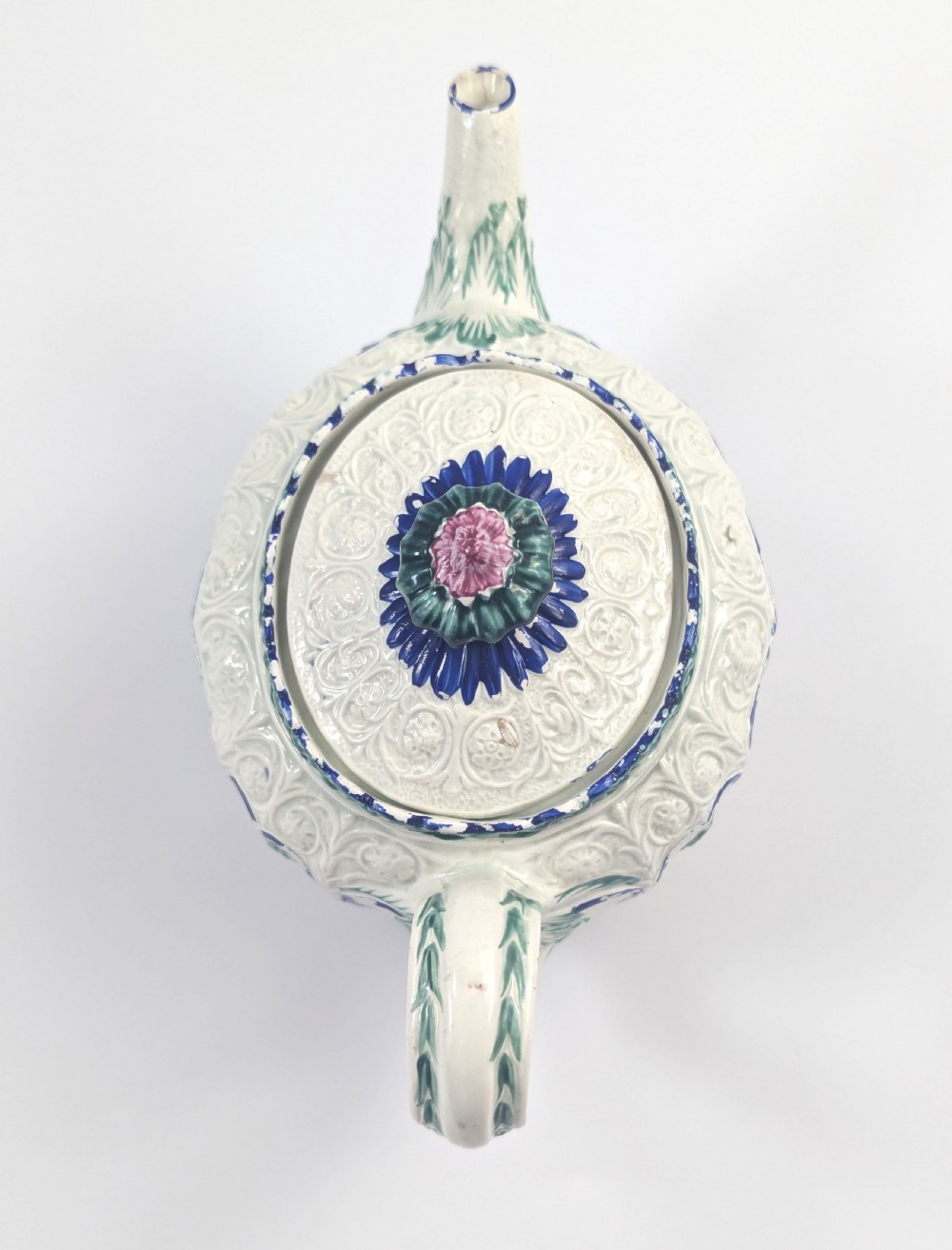 An 18th-century lead-glazed ceramic teapot featuring relief-moulded arches, blue and green painted accents, and a moulded lid with a pink flower finial. View IX