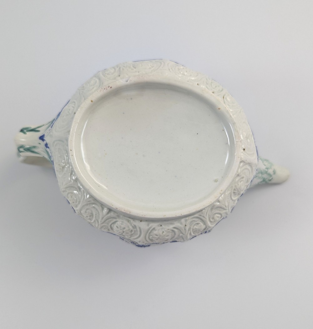 An 18th-century lead-glazed ceramic teapot featuring relief-moulded arches, blue and green painted accents, and a moulded lid with a pink flower finial. View XI