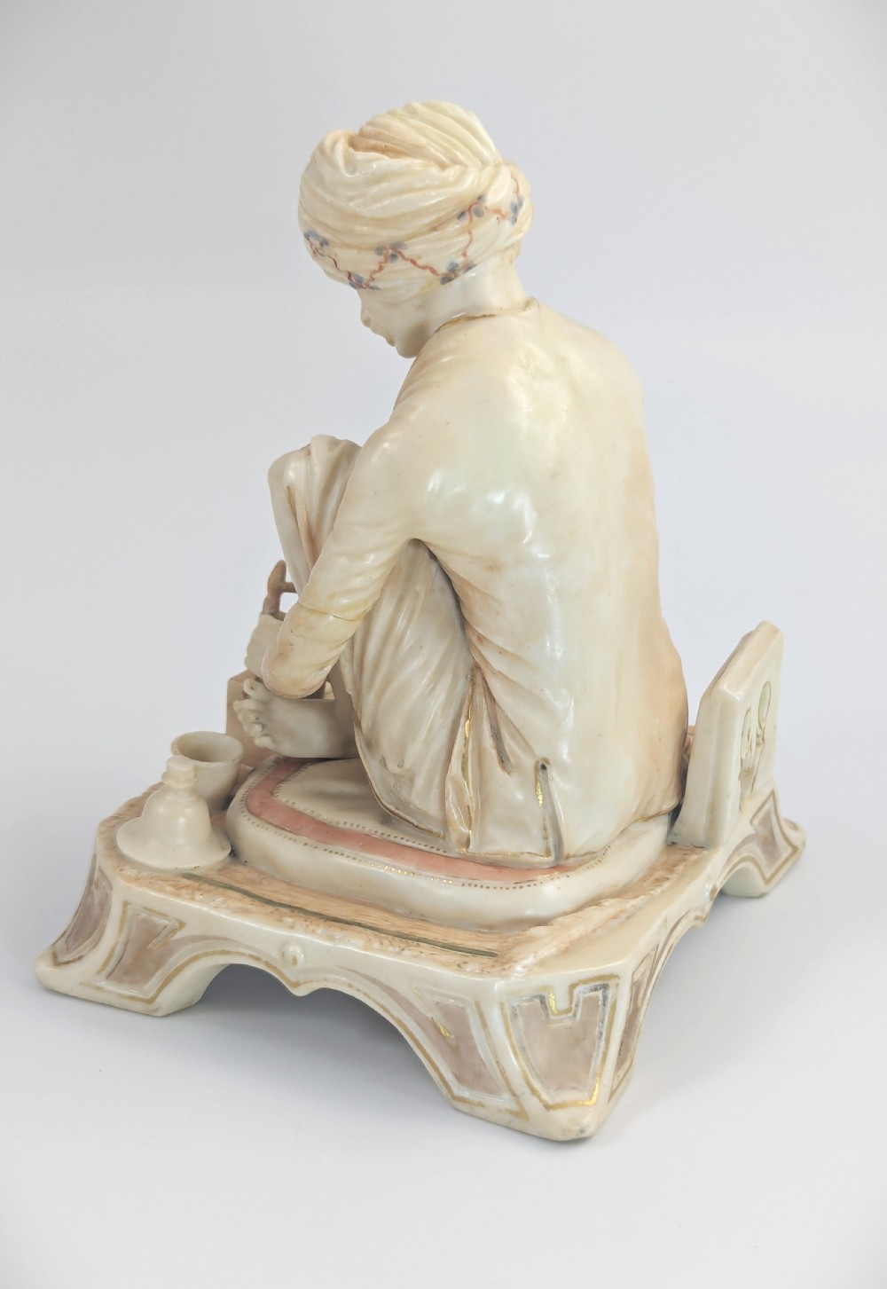 A late nineteenth-century Royal Worcester blush ivory porcelain figurine depicting a seated Indian craftsman working on an ornate pedestal base. View III