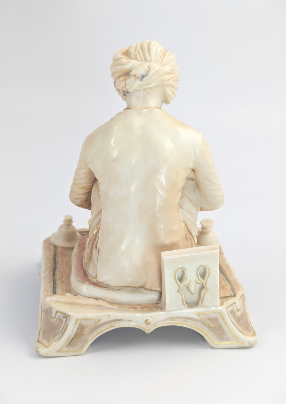 A late nineteenth-century Royal Worcester blush ivory porcelain figurine depicting a seated Indian craftsman working on an ornate pedestal base. View IV