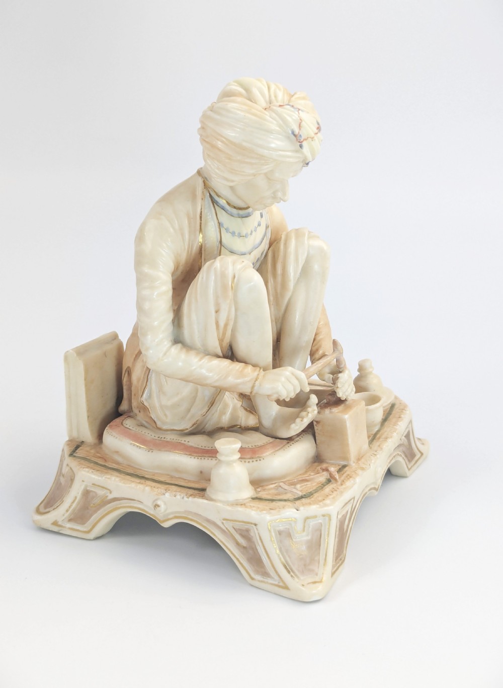 A late nineteenth-century Royal Worcester blush ivory porcelain figurine depicting a seated Indian craftsman working on an ornate pedestal base. View VI