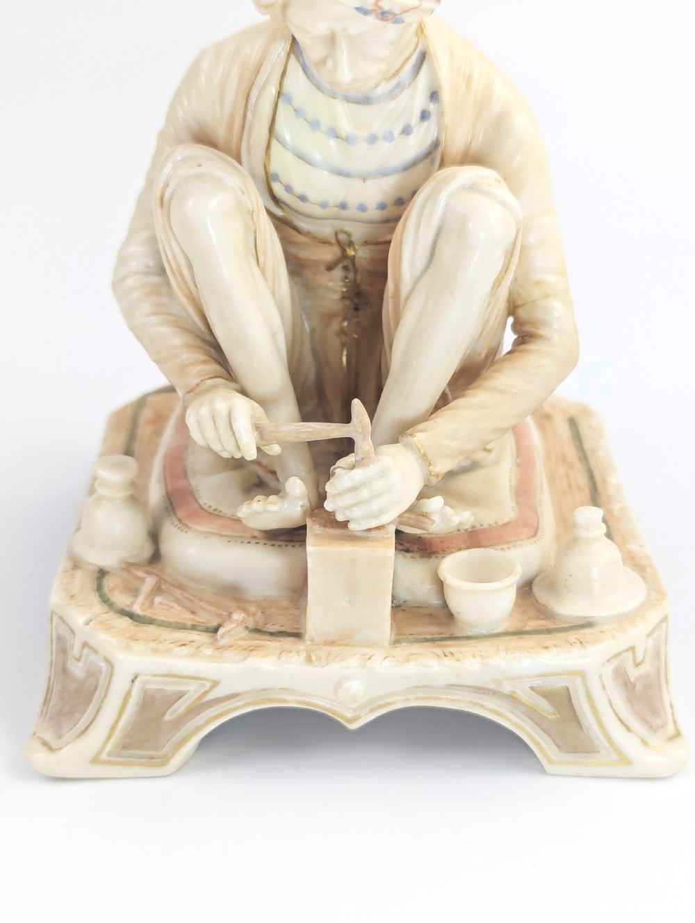 A late nineteenth-century Royal Worcester blush ivory porcelain figurine depicting a seated Indian craftsman working on an ornate pedestal base. View VII