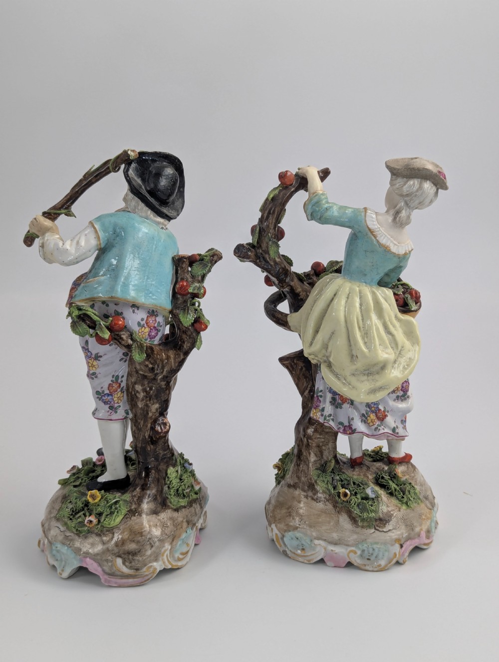 A pair of 18th-century German porcelain figurines depicting a male and female gardener standing beside fruiting trees on Rococo scrollwork bases. View III