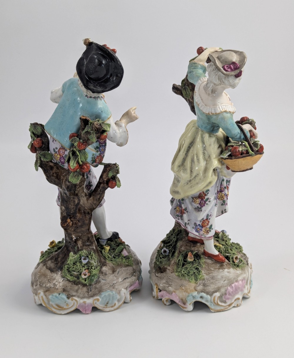 A pair of 18th-century German porcelain figurines depicting a male and female gardener standing beside fruiting trees on Rococo scrollwork bases. View IV