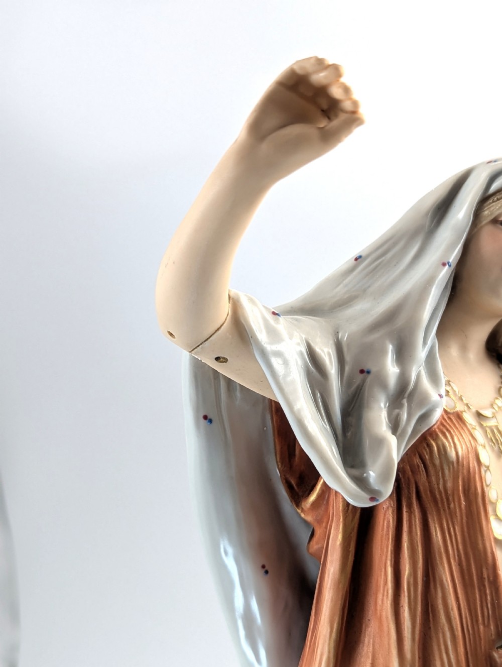 An antique Royal Dux porcelain figurine depicting a standing young woman wearing draped terracotta and cream robes on a decorative rocky pedestal. View X