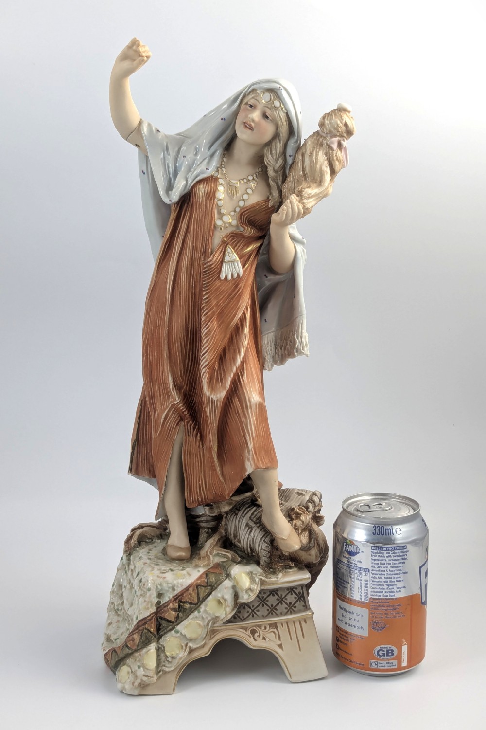 An antique Royal Dux porcelain figurine depicting a standing young woman wearing draped terracotta and cream robes on a decorative rocky pedestal. View XII