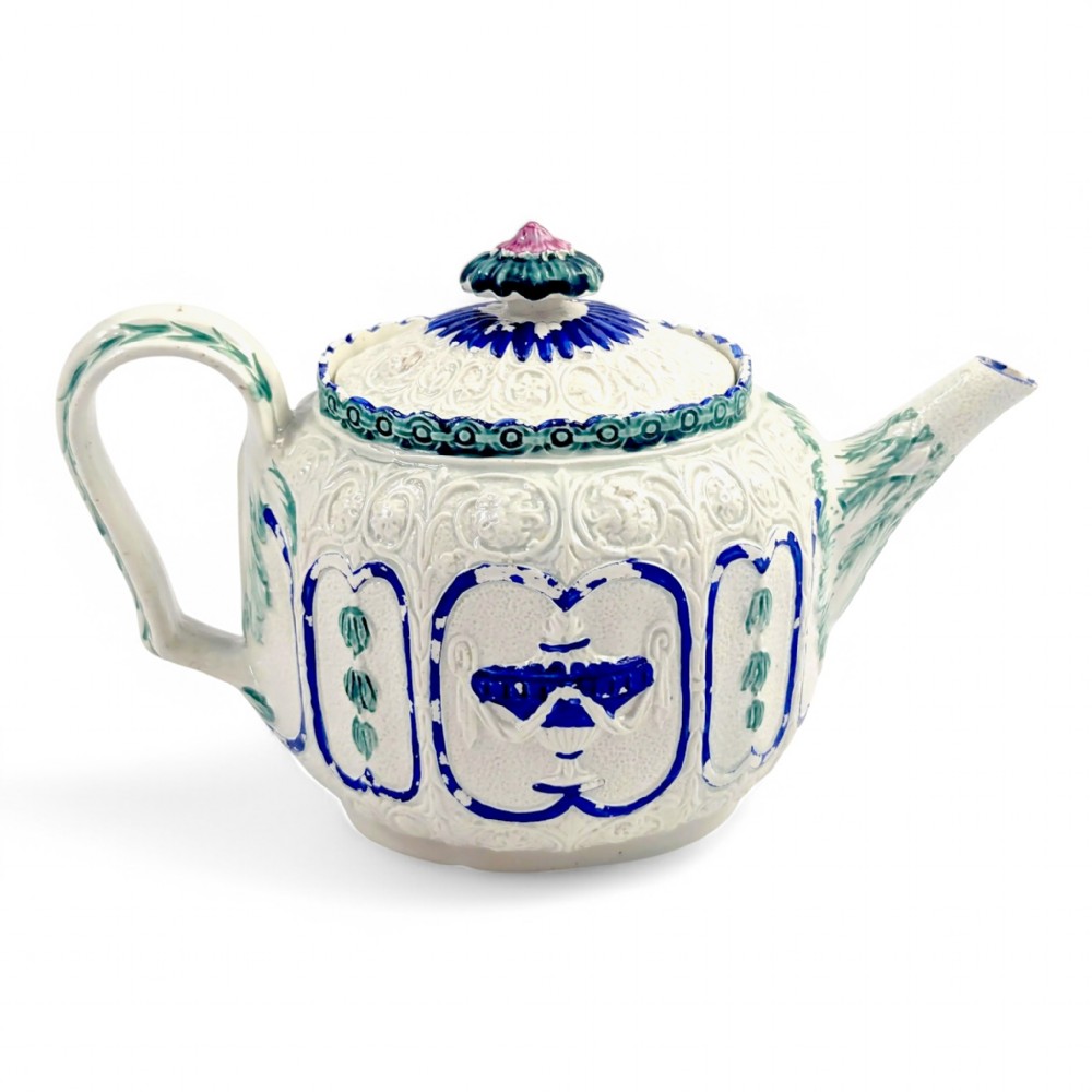 An 18th-century lead-glazed ceramic teapot featuring relief-moulded arches, blue and green painted accents, and a moulded lid with a pink flower finial.