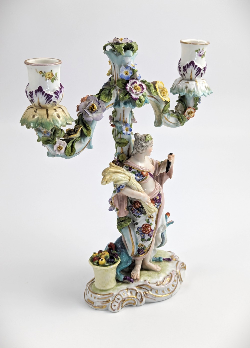 A nineteenth-century Dresden porcelain three-light candelabra featuring a central allegorical figure draped in floral fabric standing on a gilded Rococo base surrounded by encrusted porcelain flowers. View V