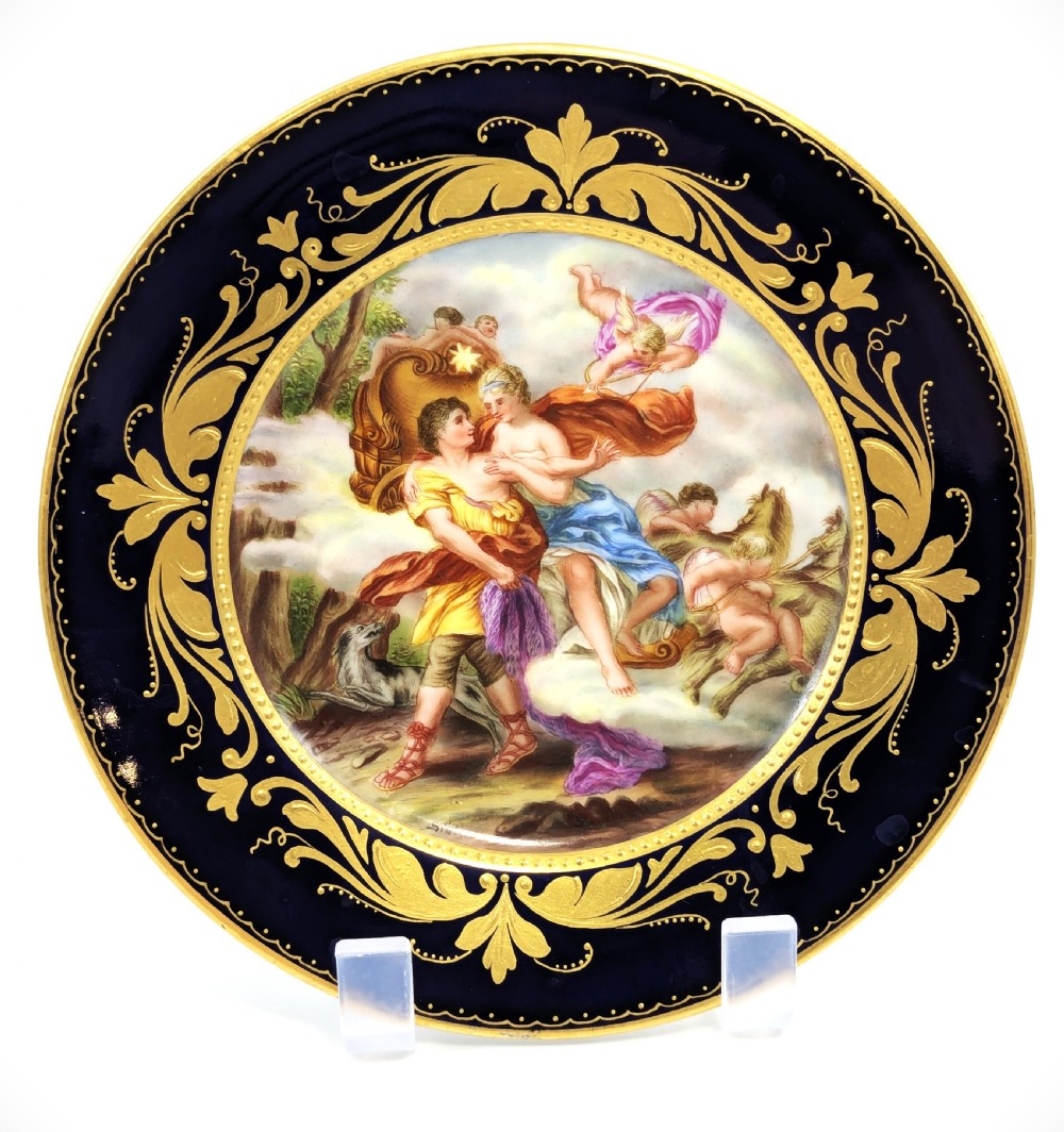 A circular porcelain cabinet plate featuring a central hand-painted scene of Aurora and Cephalus framed by a wide cobalt blue border with intricate gold scrollwork gilding. View II