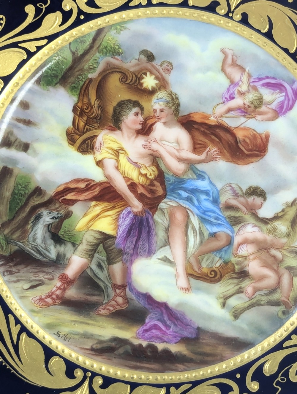 A circular porcelain cabinet plate featuring a central hand-painted scene of Aurora and Cephalus framed by a wide cobalt blue border with intricate gold scrollwork gilding. View VIII